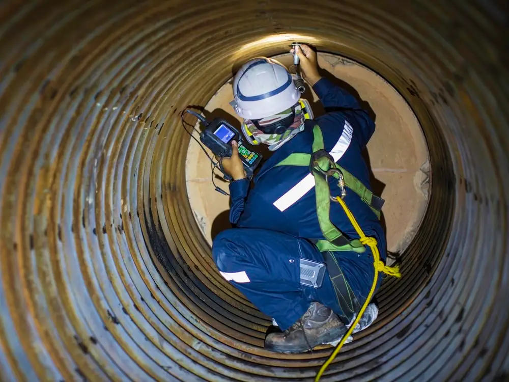 Confined-space technician inspecting the inside of a pipe